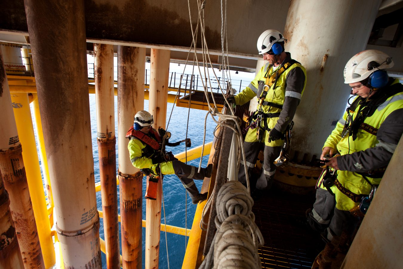 Tre klatrere i arbeid på en plattform i Nordsjøen. En er i ferd med å fire seg ned langs konduktorene for å inspisere en reparert skade.  Foto: Roger Hardy/Samfoto